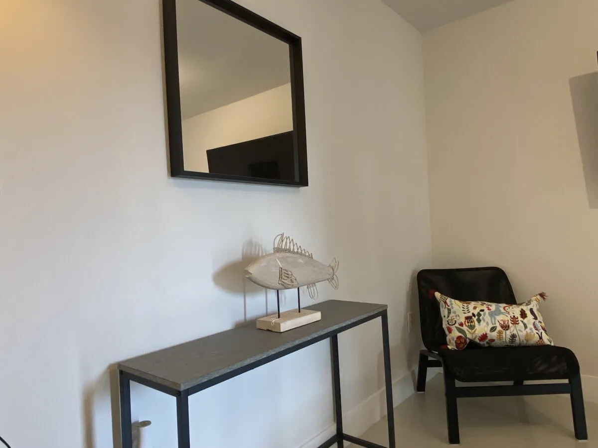 A cozy nook in the entry area featuring a black-framed mirror, a decorative fish sculpture, and a black chair with a colorful pillow. The space feels like the first impression as you enter, offering a welcoming, stylish touch right inside the door.